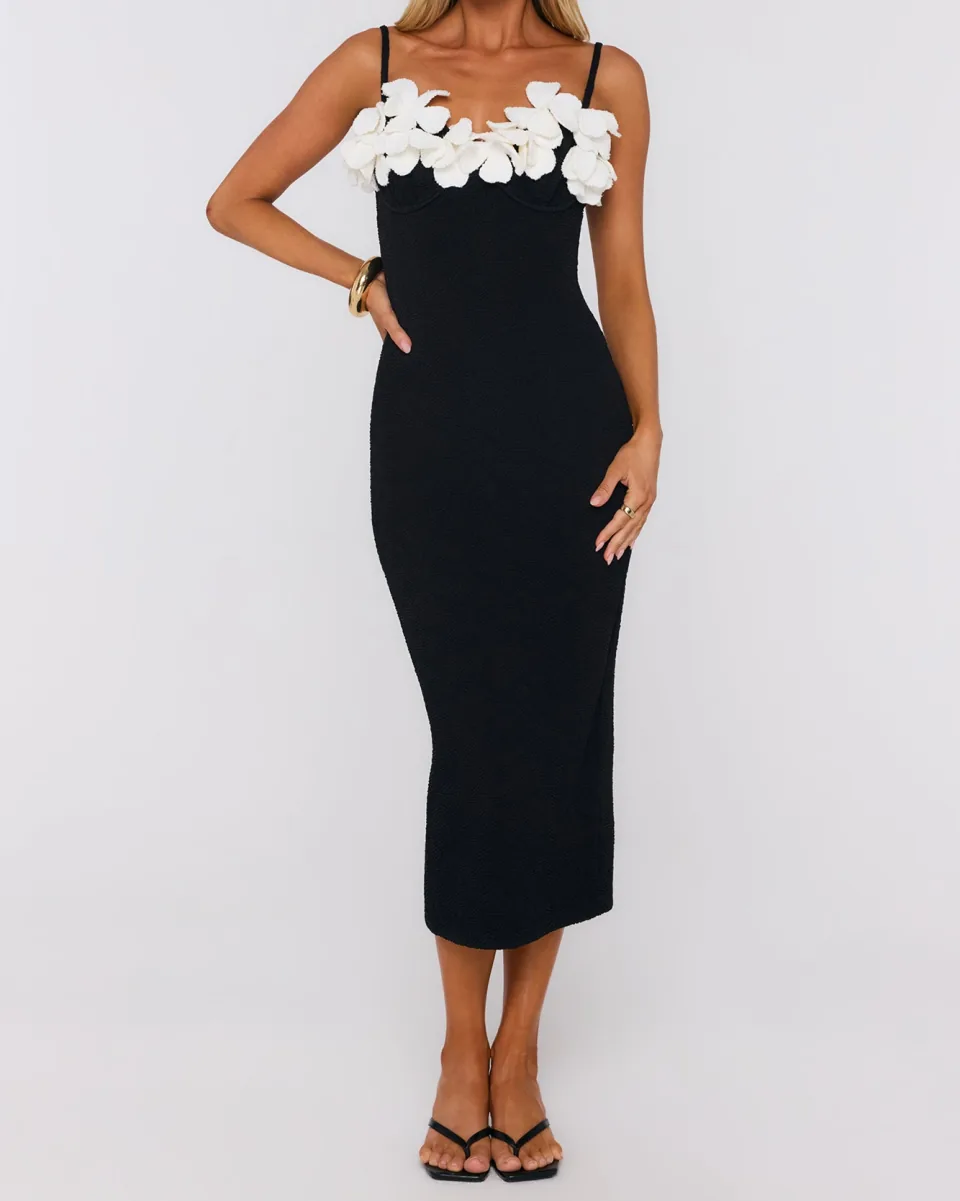 A black midi dress on thin straps, with white three-dimensional flowers along the neckline.