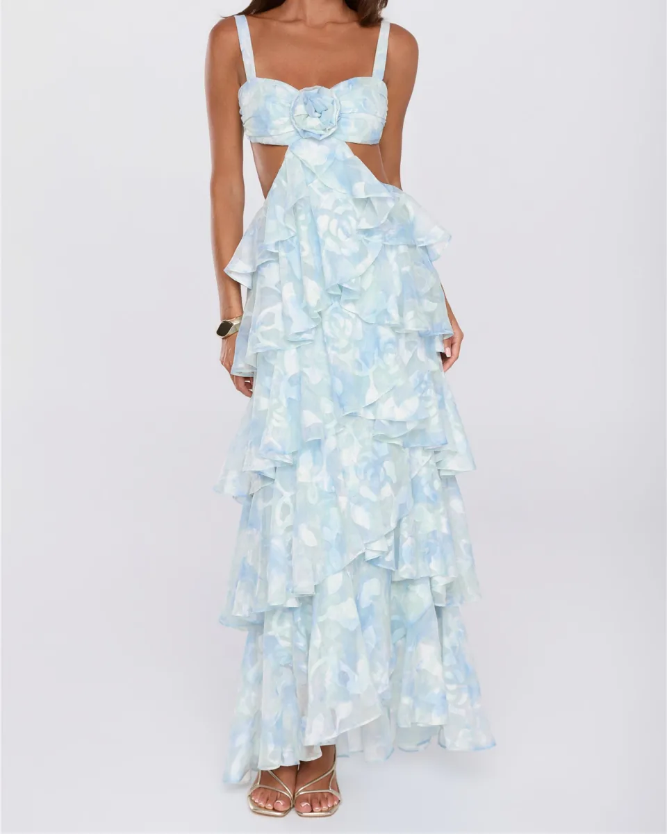 A pale blue and white printed maxi dress with a rosette at the bust, side cut-outs and a tiered ruffle skirt.