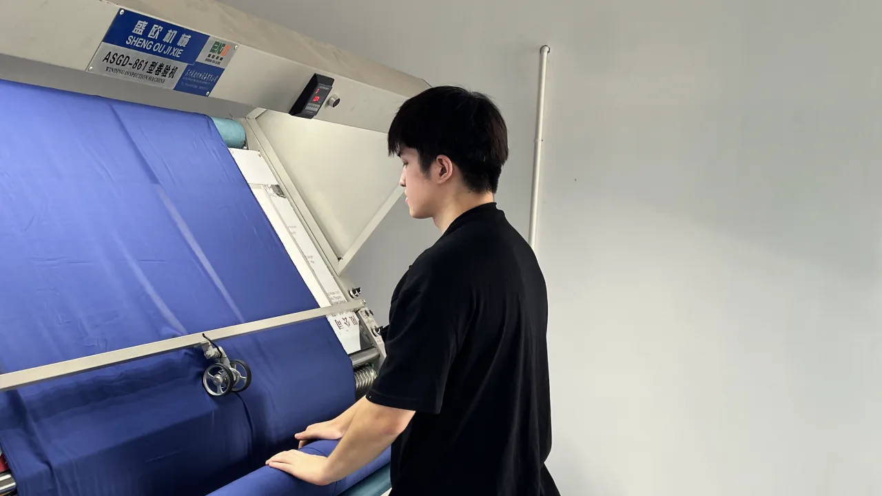 A worker running blue fabric through an inspection machine.