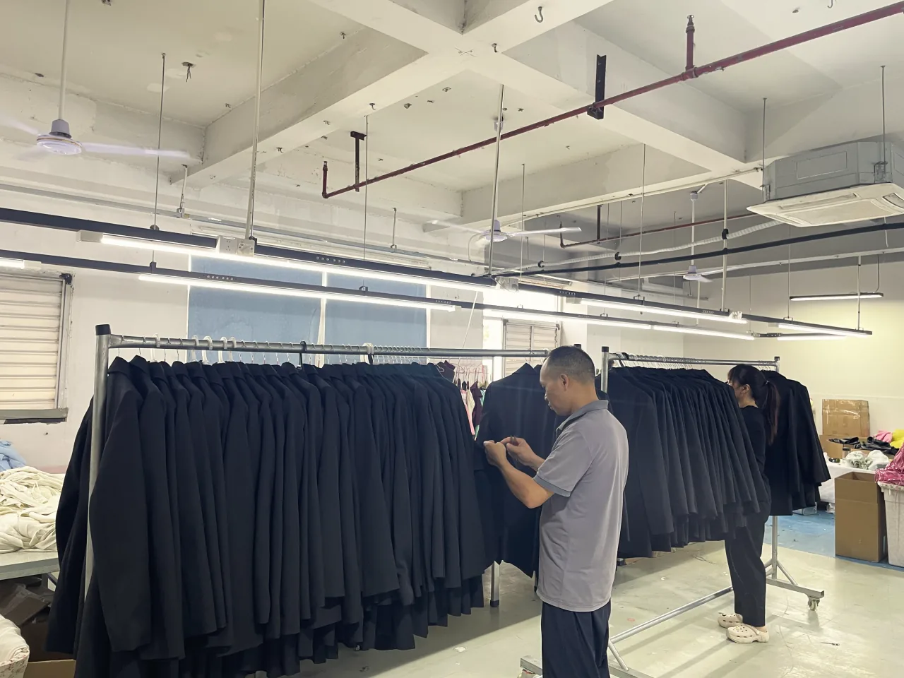 A worker checking black garments hanging on a rail.