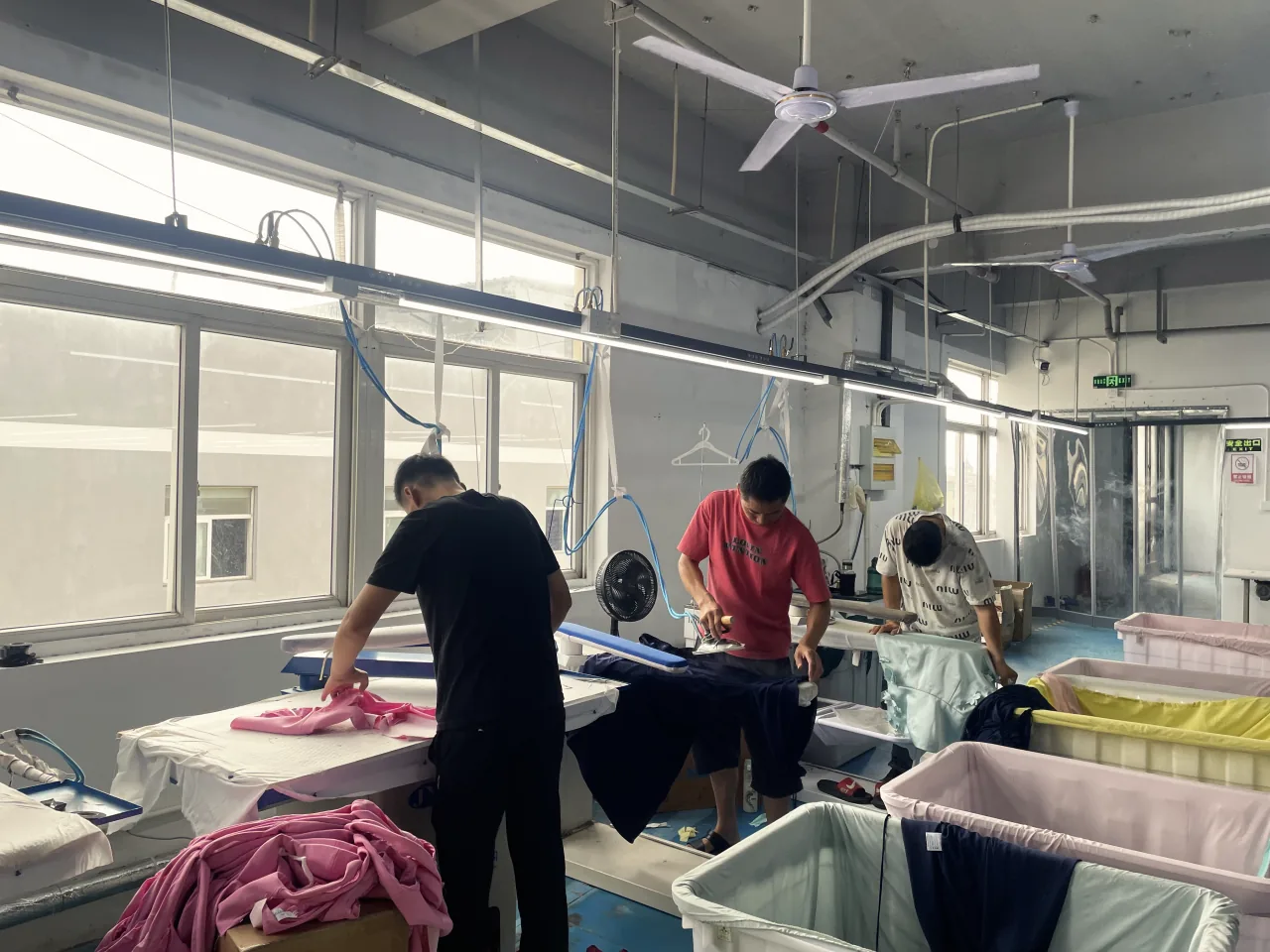 Three workers pressing garments at their boards.