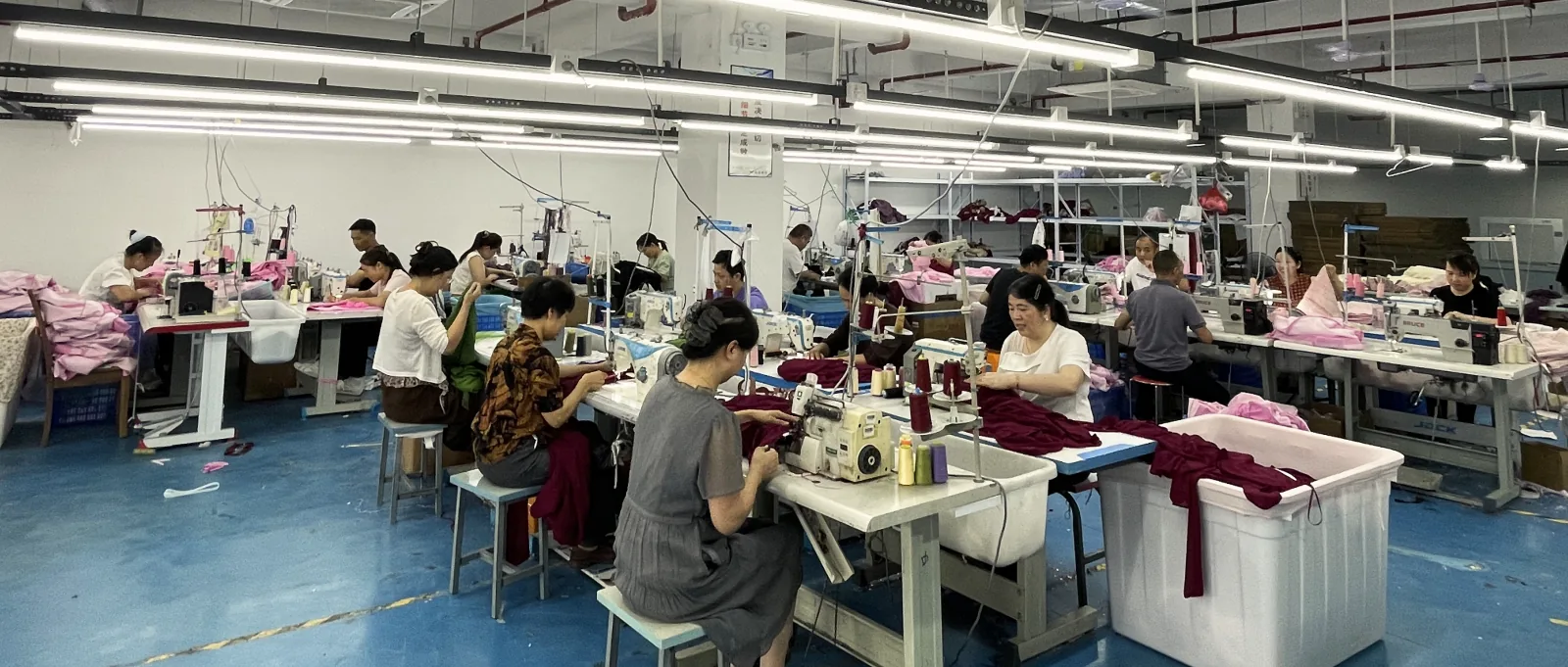 Rows of machinists at work on the sewing floor, with burgundy and pink pieces on the tables.